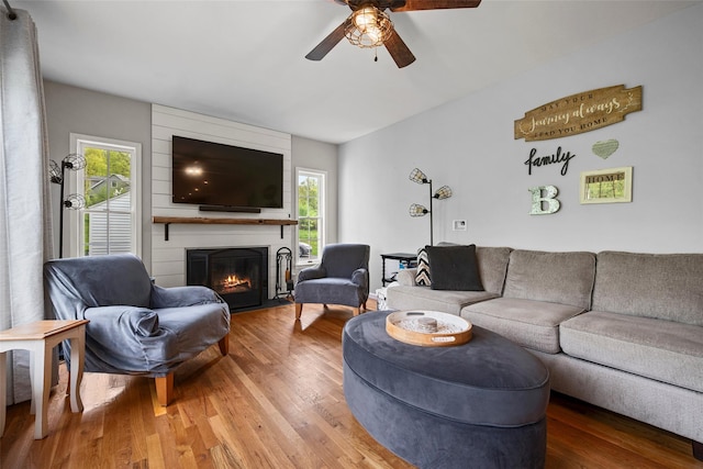 living area featuring a large fireplace, a ceiling fan, and light wood-type flooring