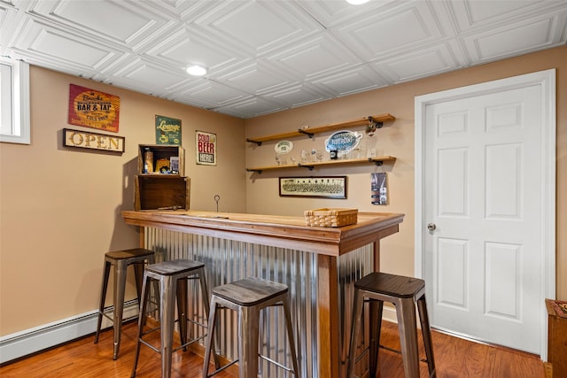 bar with a bar, wood finished floors, baseboard heating, and an ornate ceiling