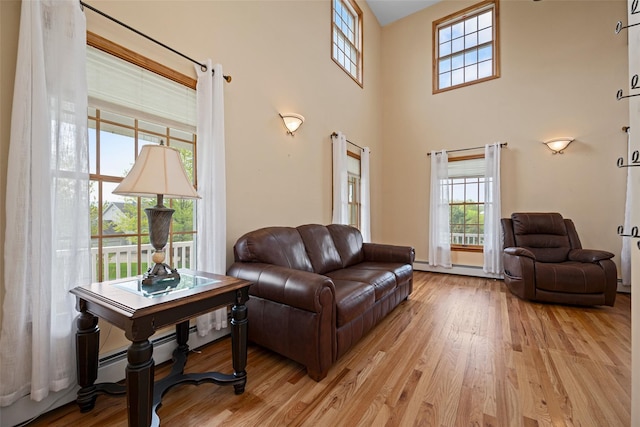living area featuring a healthy amount of sunlight, a high ceiling, a baseboard heating unit, and light wood-type flooring