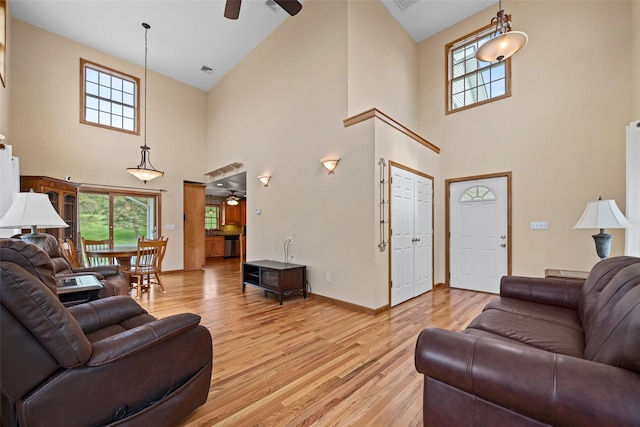 living area with light wood-type flooring, a towering ceiling, ceiling fan, and baseboards