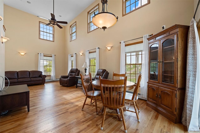 dining space featuring ceiling fan, light wood-style flooring, and a towering ceiling
