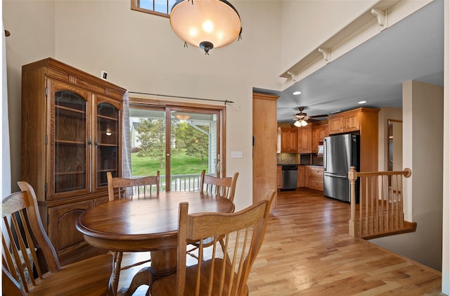 dining space featuring light wood-type flooring, a towering ceiling, and ceiling fan