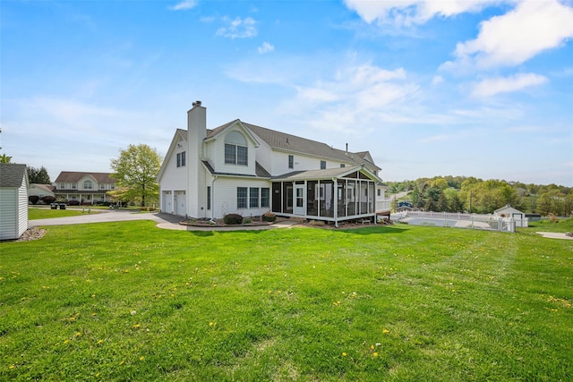 rear view of house with driveway, a chimney, a sunroom, fence, and an attached garage