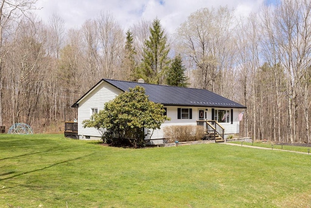 single story home with metal roof, a front lawn, and a view of trees