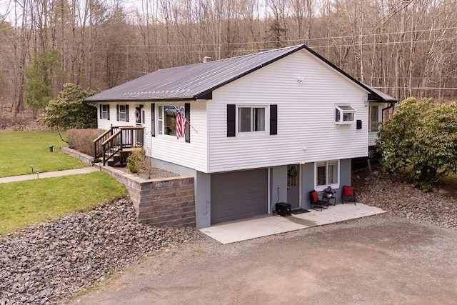 view of front of home featuring a front lawn, metal roof, driveway, a view of trees, and an attached garage