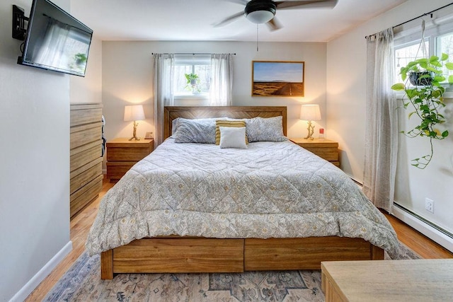 bedroom featuring baseboard heating, wood finished floors, and multiple windows