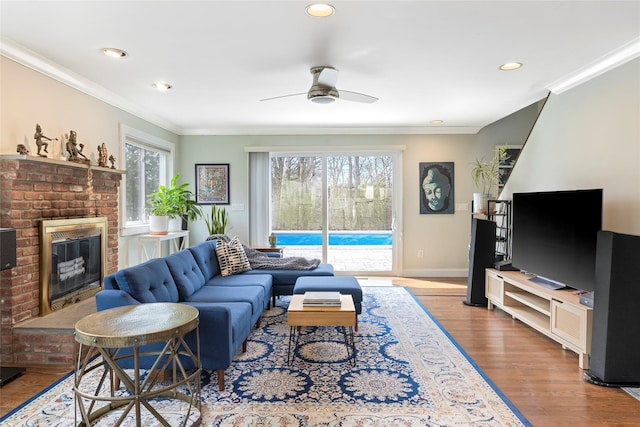 living room with recessed lighting, a fireplace, crown molding, a ceiling fan, and wood finished floors