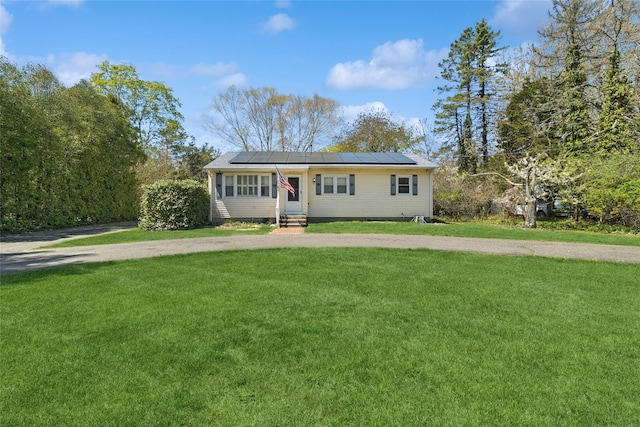 ranch-style home featuring roof mounted solar panels, entry steps, driveway, and a front lawn