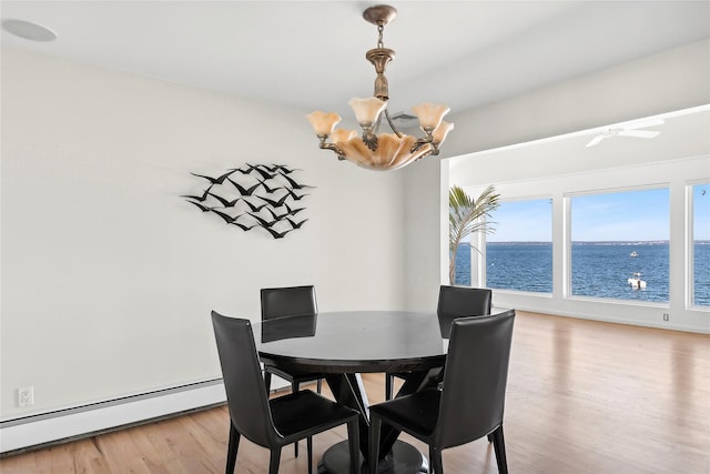 dining space with light wood-type flooring, an inviting chandelier, a water view, and a baseboard radiator