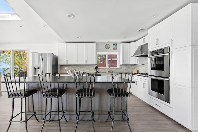 kitchen featuring under cabinet range hood, appliances with stainless steel finishes, dark countertops, backsplash, and visible vents