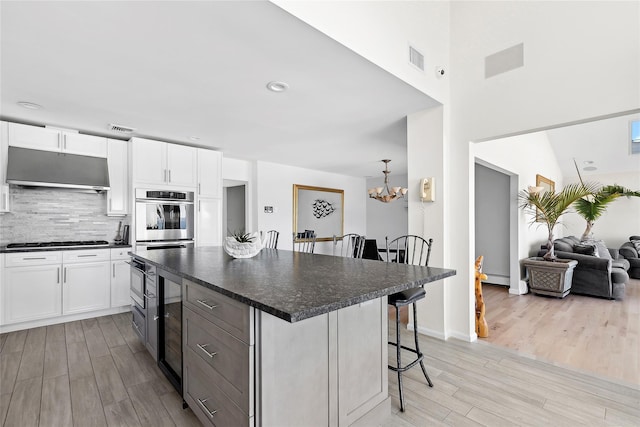 kitchen featuring light wood finished floors, under cabinet range hood, a kitchen breakfast bar, gas cooktop, and dark countertops