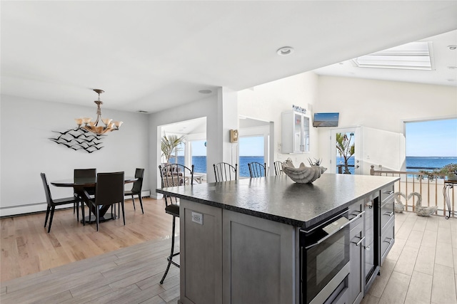 kitchen with built in microwave, a chandelier, light wood-style floors, a breakfast bar area, and dark countertops