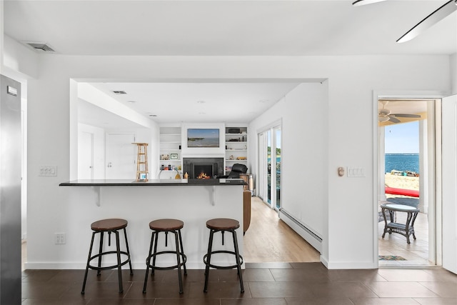 kitchen with dark countertops, a kitchen bar, a warm lit fireplace, and a baseboard heating unit