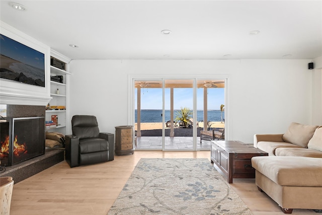 living area featuring recessed lighting, a water view, light wood-style floors, and a fireplace