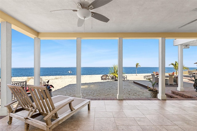 sunroom featuring a textured ceiling, a beach view, and a water view