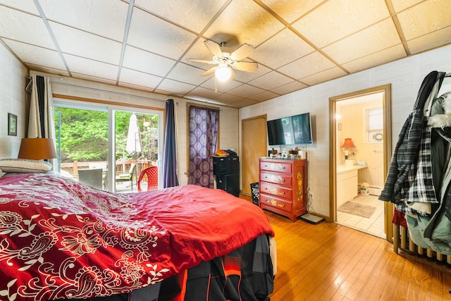 bedroom featuring a drop ceiling, wood-type flooring, access to exterior, ensuite bath, and ceiling fan