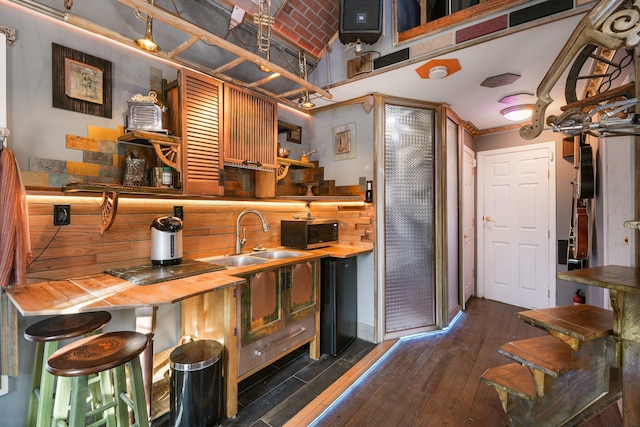 bar with a sink, dark wood finished floors, vaulted ceiling, and stainless steel microwave
