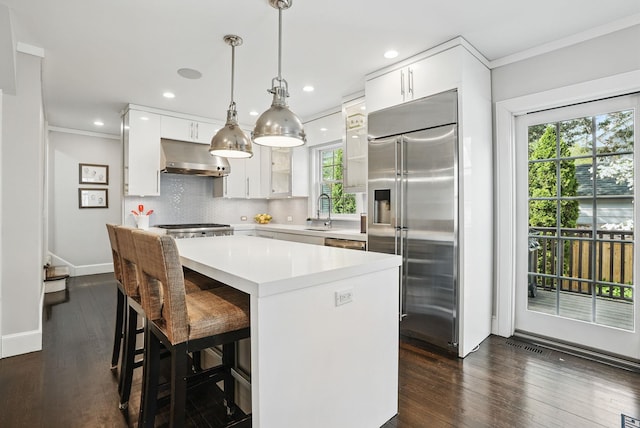 kitchen with light countertops, under cabinet range hood, stainless steel built in fridge, white cabinets, and backsplash