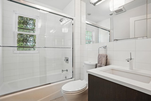 full bath featuring tile walls, tasteful backsplash, vanity, toilet, and shower / bath combination with glass door