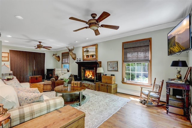 living room featuring a ceiling fan, ornamental molding, a brick fireplace, recessed lighting, and light wood-style floors