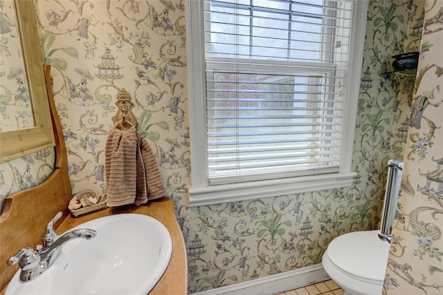 half bathroom featuring wallpapered walls, a sink, toilet, and baseboards