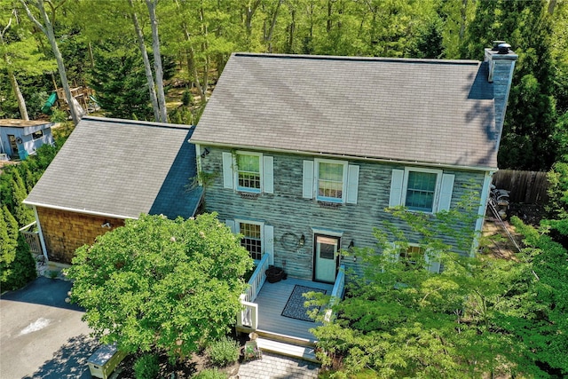 view of front of house featuring a chimney, a deck, a wooded view, and fence