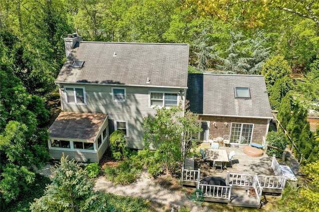 back of house featuring a chimney, a wooden deck, a forest view, and outdoor dining space