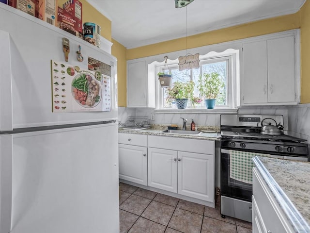 kitchen with freestanding refrigerator, stainless steel gas range oven, light countertops, white cabinets, and a sink