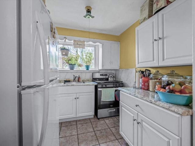 kitchen with gas stove, freestanding refrigerator, light tile patterned floors, a sink, and white cabinetry