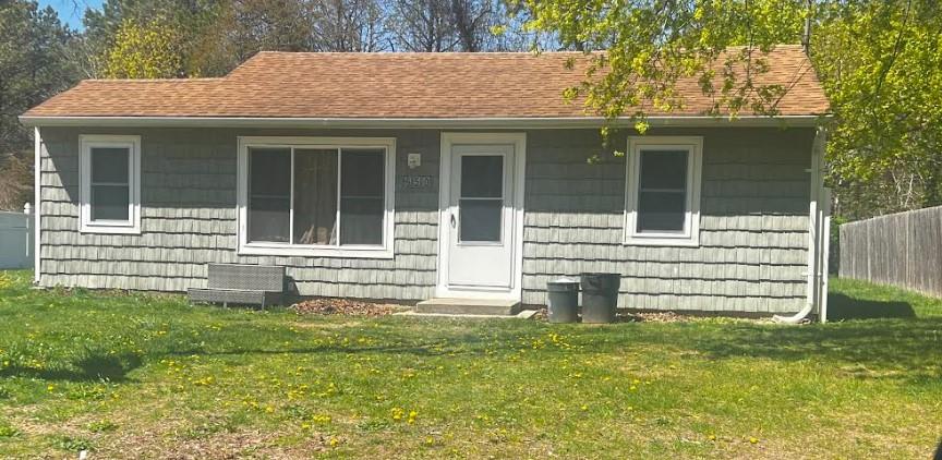view of front facade featuring fence, a shingled roof, and a front yard