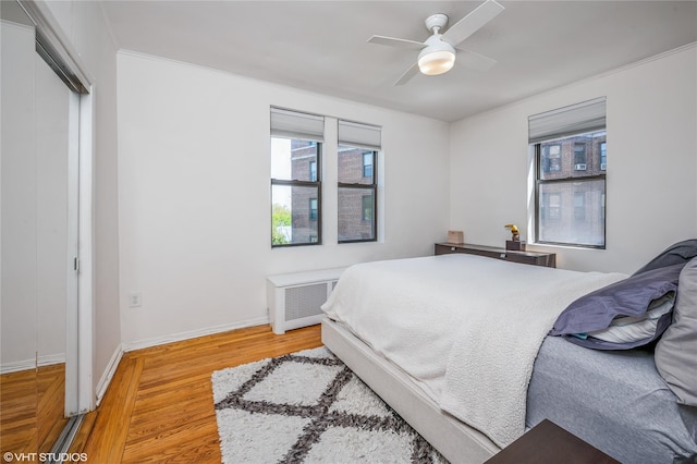 bedroom featuring a ceiling fan, light wood-type flooring, baseboards, a closet, and radiator