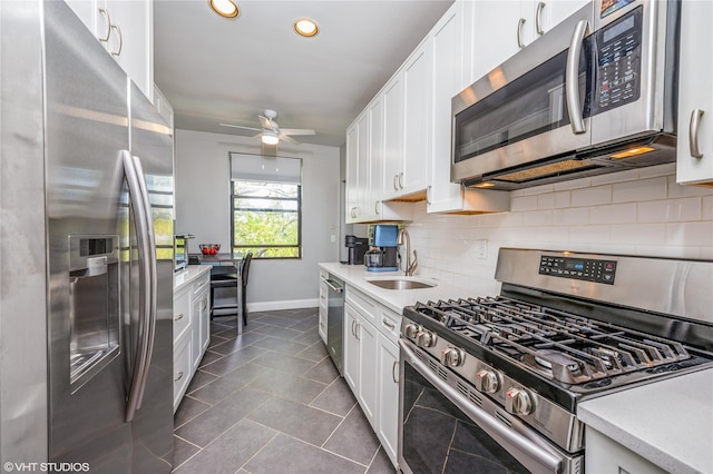 kitchen with baseboards, light countertops, a sink, appliances with stainless steel finishes, and backsplash