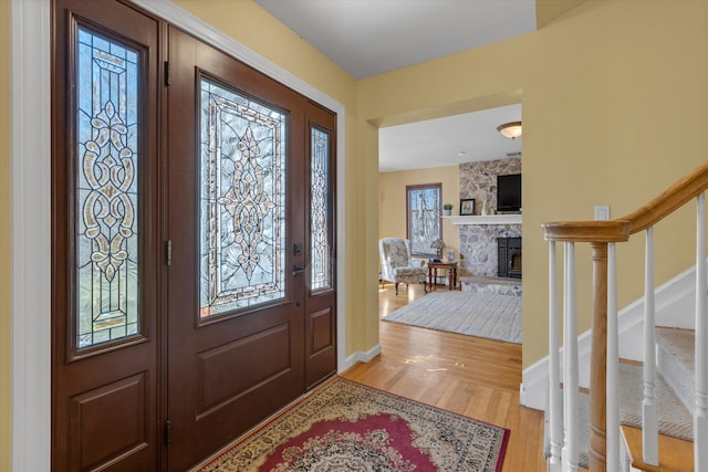 foyer entrance featuring baseboards, light wood-type flooring, a stone fireplace, and stairs