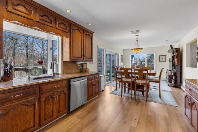 kitchen with pendant lighting, dishwasher, a sink, light stone counters, and light wood finished floors