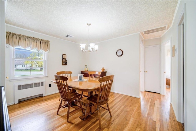 dining area with a textured ceiling, visible vents, light wood-style flooring, and radiator
