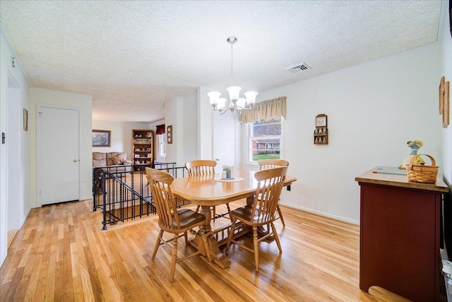 dining space with visible vents, a textured ceiling, light wood-style flooring, and a chandelier