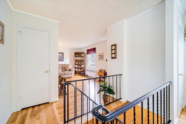 hall featuring a textured ceiling, an upstairs landing, light wood-style floors, radiator, and ornamental molding