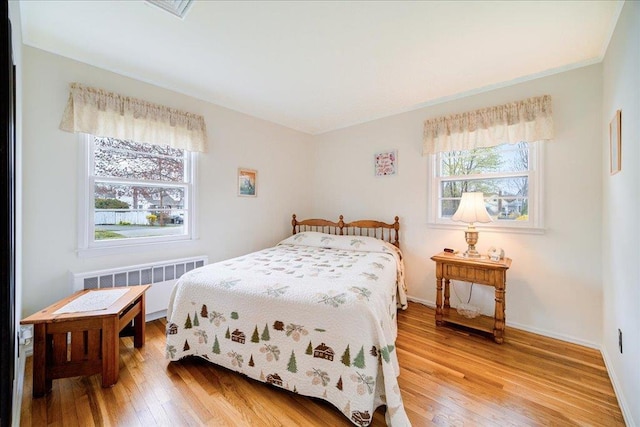 bedroom featuring radiator heating unit, baseboards, and light wood finished floors