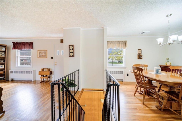 dining room featuring light wood-style floors, radiator, crown molding, and a notable chandelier