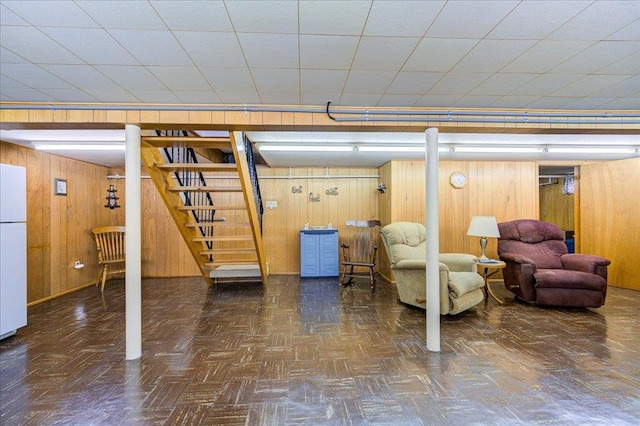 finished basement featuring freestanding refrigerator, wood walls, and stairs