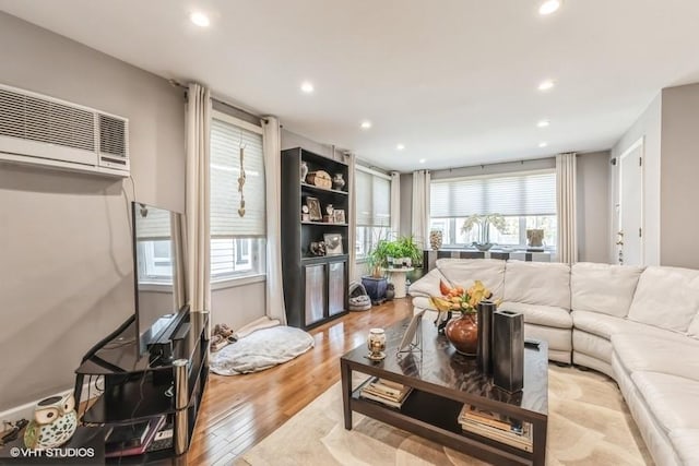 living room with a wall mounted air conditioner, a wealth of natural light, wood finished floors, and recessed lighting