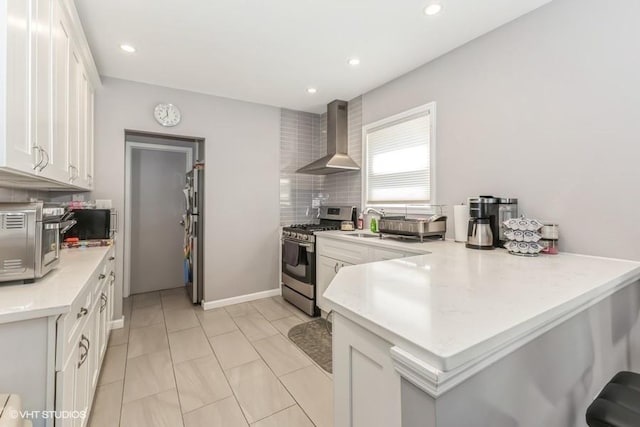 kitchen with white cabinets, stainless steel appliances, light countertops, wall chimney exhaust hood, and a peninsula