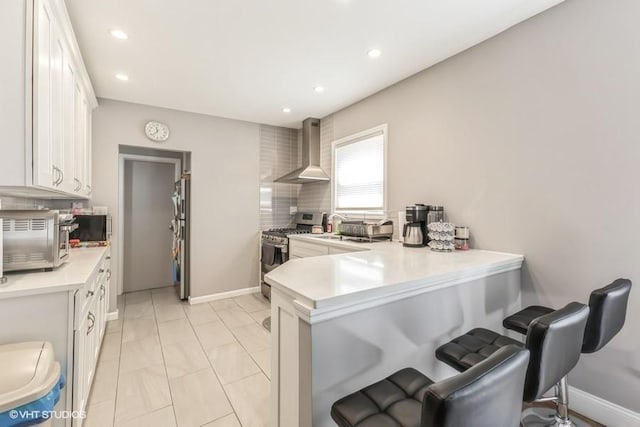 kitchen featuring a peninsula, a breakfast bar area, stainless steel appliances, light countertops, and wall chimney exhaust hood