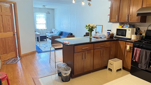 kitchen featuring under cabinet range hood, light wood-type flooring, a peninsula, white microwave, and black gas range