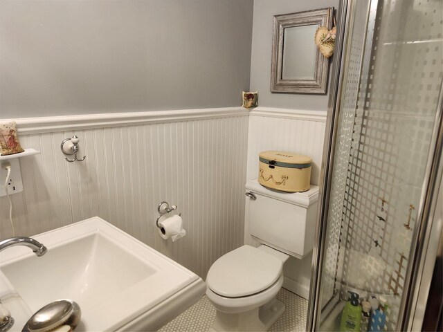 bathroom with a shower stall, a sink, a wainscoted wall, tile patterned floors, and toilet