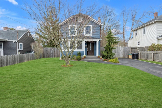 view of front of house with fence, a chimney, a front yard, and aphalt driveway