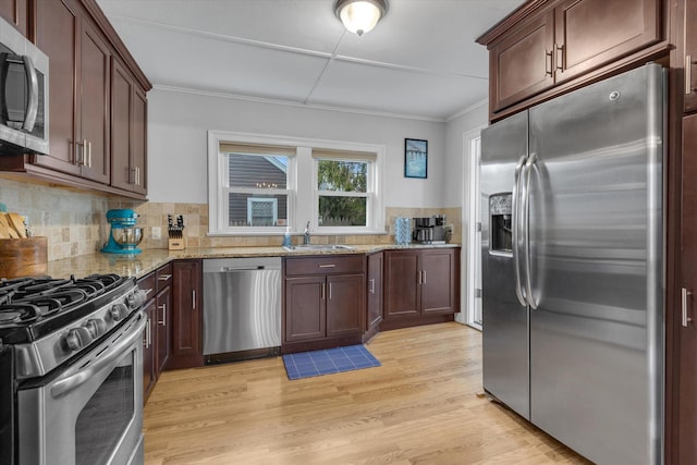 kitchen featuring crown molding, light stone countertops, a sink, backsplash, and stainless steel appliances