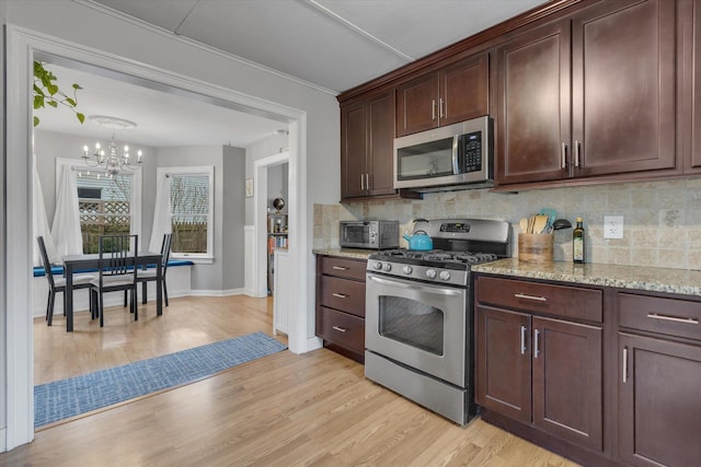 kitchen with light stone countertops, light wood-style floors, appliances with stainless steel finishes, backsplash, and a notable chandelier