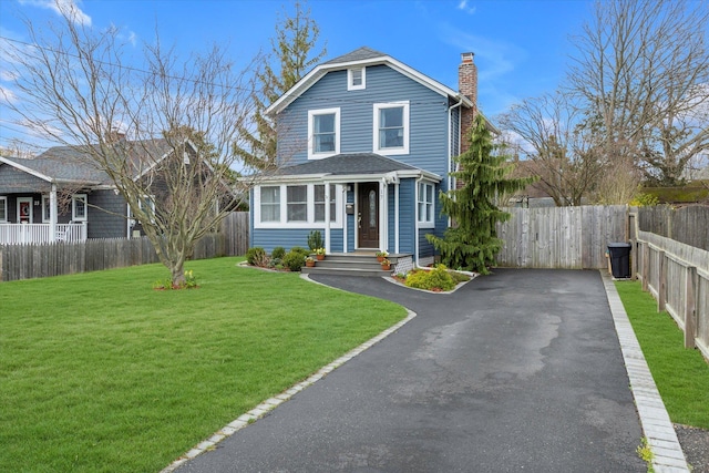 american foursquare style home featuring a front yard, fence, driveway, and a chimney