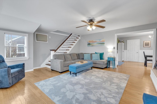 living area featuring light wood-style floors, baseboards, ceiling fan, and stairs